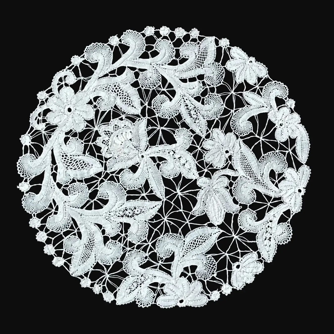 Ručno rađeni tabletić od čipke na batiće napravljen od tankog bijelog konca, u obliku kruga bogato ispunjenog zavijutcima različitih veličina i oblika cvijeća s listićima, ispunjenih različitim motivima čipke.