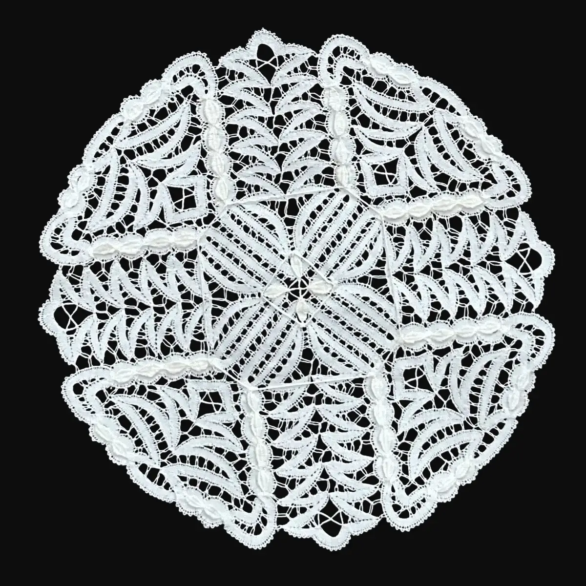 Ručno rađeni tabletić od čipke na batiće napravljen od tankog bijelog konca, u obliku kruga ispunjenog proporcionalno raspoređenim zavijutcima sa oštrim kutovima, sa dodatnim elementima na površini čipke u obliku malih listića.