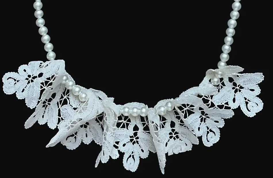 Ručno izrađena čipkana kragna izrađena u obliku malih zavijutaka od tankog krem konca koja je spojena sa ogrlicom od malih bijelih okruglih umjetnih bisera u jednu cjelinu.