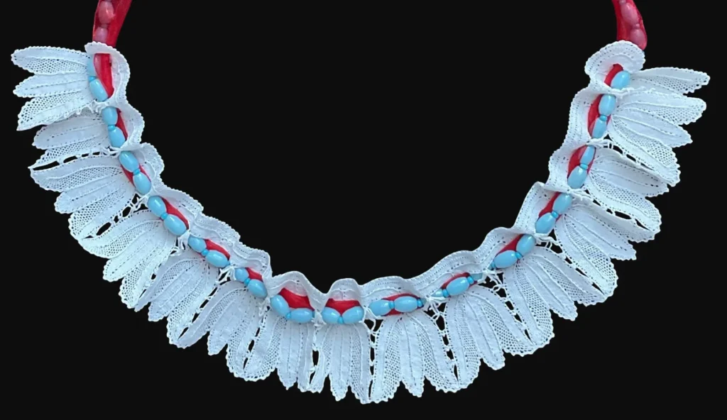 Ručno izrađena čipkana kragna kao niz tulipana izrađena od tankog bijelog konca, spojena sa ogrlicom od plavkastih umjetnih perlica sa crvenom trakom u jednu cjelinu.
